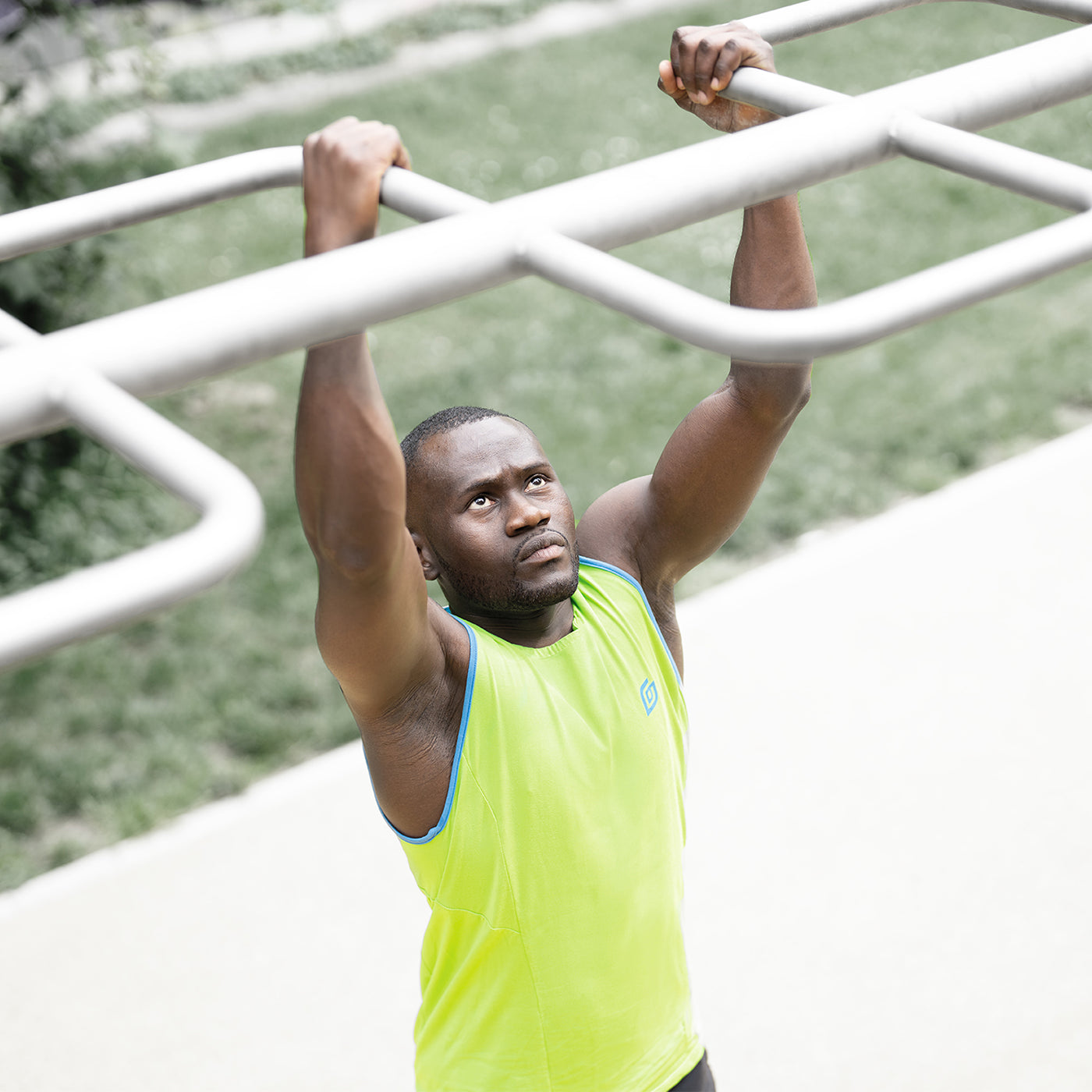 Sportler im Calisthenics Park bei der Übung: er macht Klimmzüge und er trägt dabei das KiiGO Herren Tanktop in Lime. Der Kontrast des Shirts zum HIntergrund ist stark, weil die Farben des kiiGO Shirts sehr knallig sind.